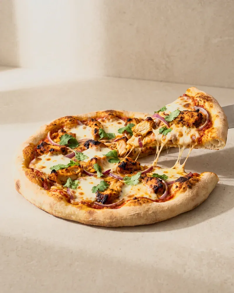 A chicken tikka pizza with a slice lifting away